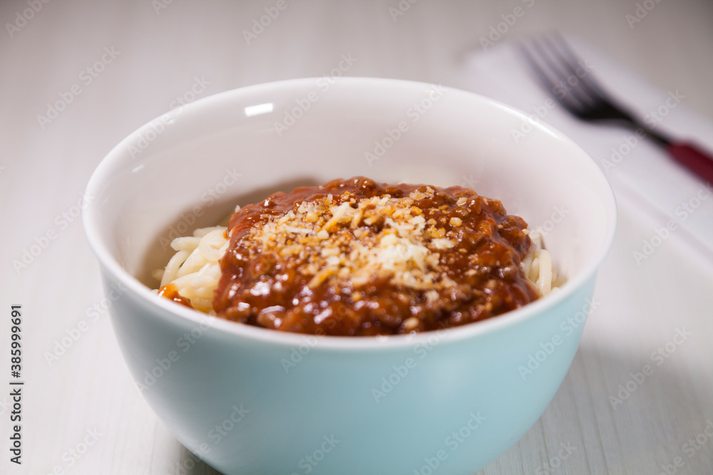 Spaghetti pasta with tomato sauce in white and blue bowl, white wooden background and resting straw plate and cutlery on the side, Brazilian cuisine copy space, top view. Food concept. Pasta concept. Spaghetti pasta with tomato sauce in white and blue bowl, white wooden background and resting straw plate and cutlery on the side, Brazilian cuisine copy space, top view. Food concept. Pasta concept.