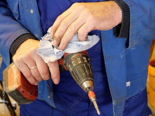 Handwerker im Blaumann reinigt Bohrmaschine mit Tuch