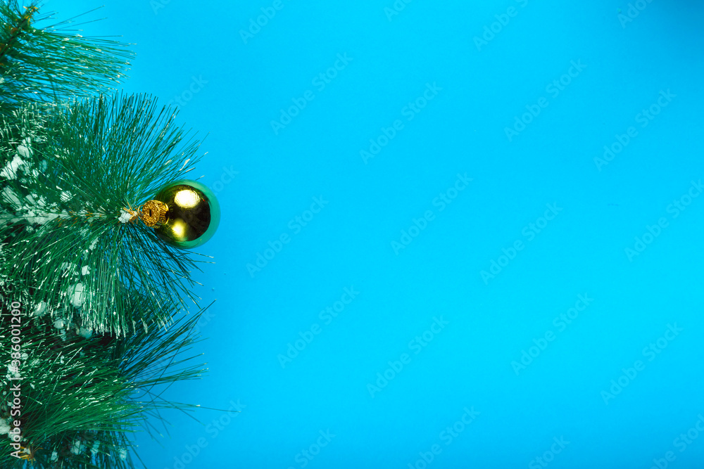 Obraz premium Pine twig in the snow with a ball decoration on a blue background.