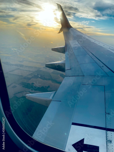View from airplane window and the wing with sunset sky over fluffy clouds, flying and traveling concept background (ID: 386002267)