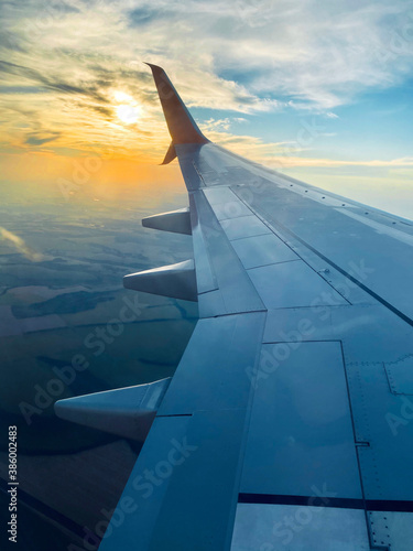 View from airplane window and the wing with sunset sky over fluffy clouds, flying and traveling concept background (ID: 386002483)