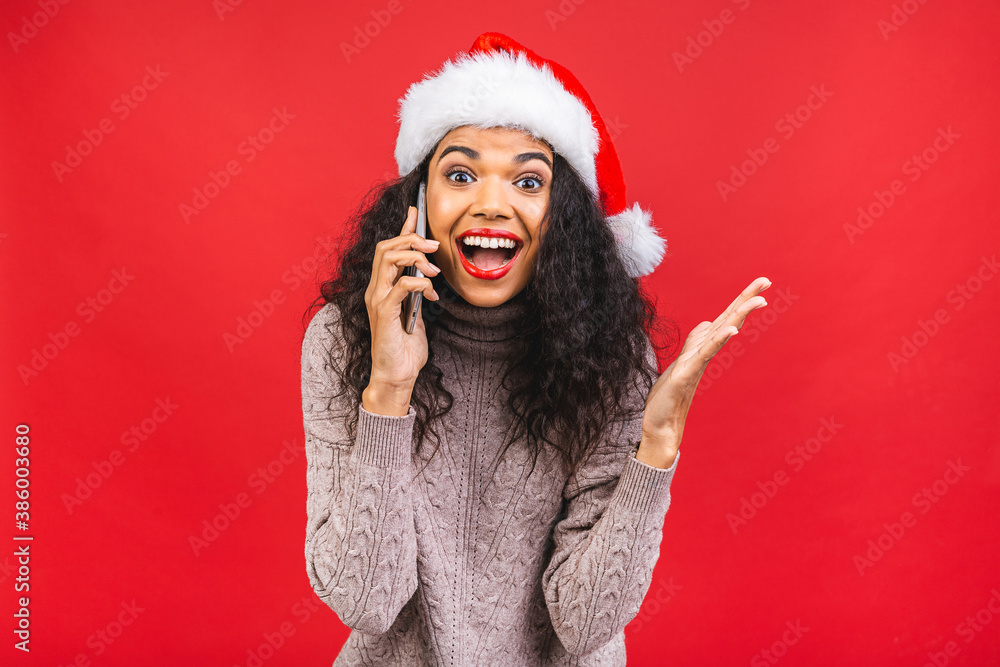 Happy excited african american woman in red santa claus hat with mobile phone isolated over red background. Happy excited african american woman in red santa claus hat with mobile phone isolated over red background.