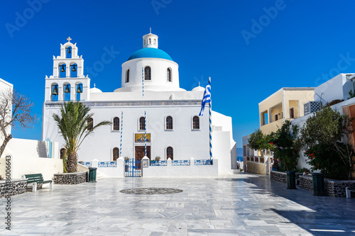 Orthodox church in Oia, Santorini, Greece on a summer day with greek flag. beautiful clear blue sky. empty square, summer 2020, during coronavirus pandemic