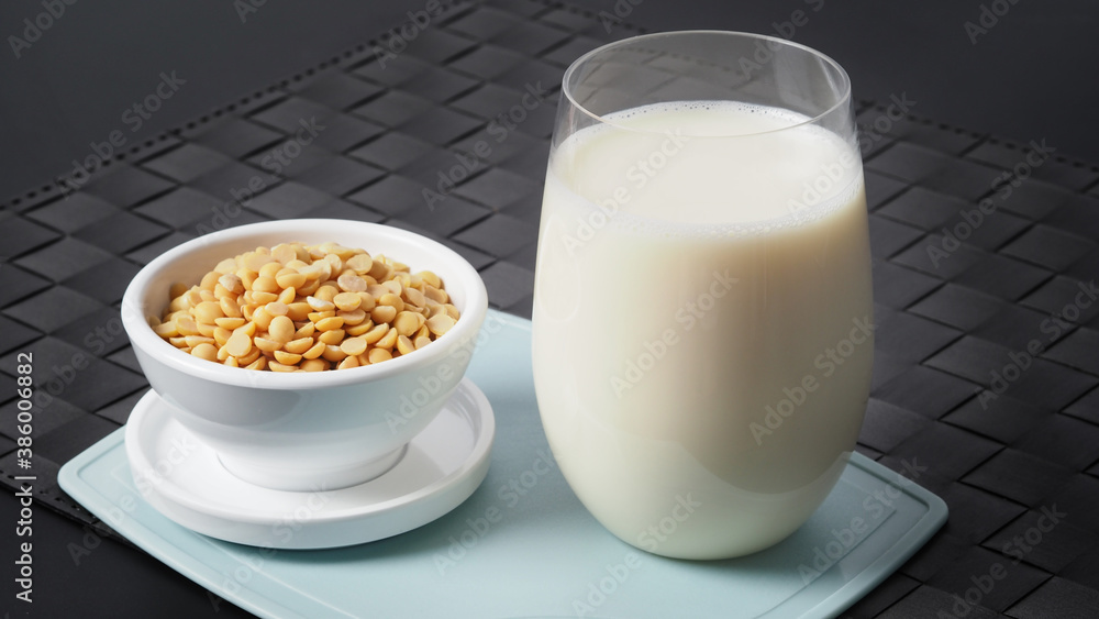 Close-up images of home made healthy drink soy milk with no sugar added in a glass on a green color plastic plate mat and soy beans in small bowl. All of them on black background in a studio shot. Close-up images of home made healthy drink soy milk with no sugar added in a glass on a green color plastic plate mat and soy beans in small bowl. All of them on black background in a studio shot.