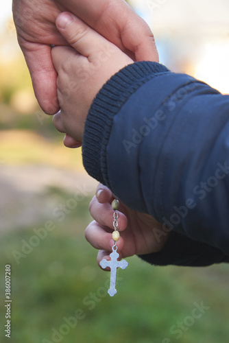 Dad and little son hold each other's hand with a rosary.