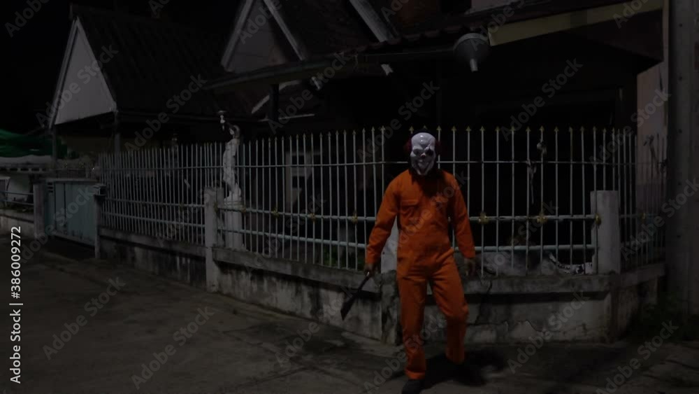 Asian handsome man wear clown mask with weapon at the night scene,Halloween festival concept,Horror scary photo of a killer in orange cloth Asian handsome man wear clown mask with weapon at the night scene,Halloween festival concept,Horror scary photo of a killer in orange cloth