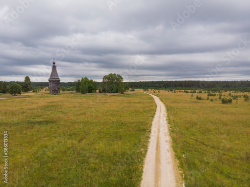 August, 2020 - Red Lag. Abandoned tall wooden church in the middle of a large field. Russia, Arkhangelsk region 