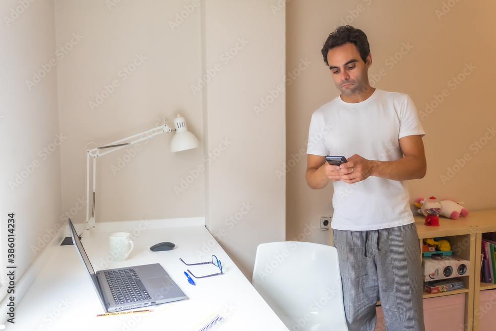 businessman standing with his mobile phone working at home in home clothes while answering messages businessman standing with his mobile phone working at home in home clothes while answering messages