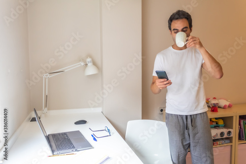 businessman standing with his mobile phone working at home in home clothes while answering messages and having a cup of coffee