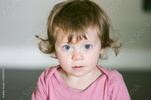 Close up Portrait of Cute 18 Month Old Baby Girl with big blue Eyes and Curly Brown Hair. Toddler's Funny Face Expression. 