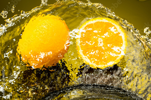 Fototapeta Naklejka Na Ścianę i Meble -  two oranges, whole and cut in half with drops and splashes of water on dark glass with gradient background and reflection