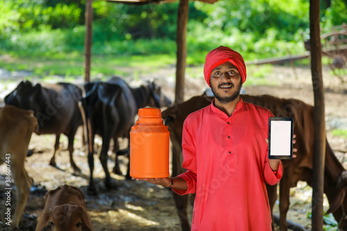 Indian farmer holding milk bottle in hand and showing mobile phone blank screen