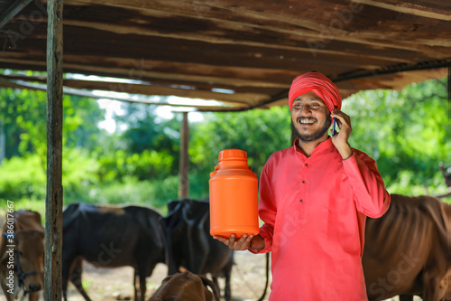 Indian farmer holding milk bottle and using smart phone at dairy farm