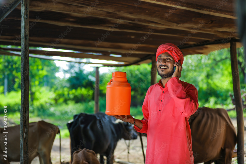 Indian farmer holding milk bottle and using smart phone at dairy farm Indian farmer holding milk bottle and using smart phone at dairy farm