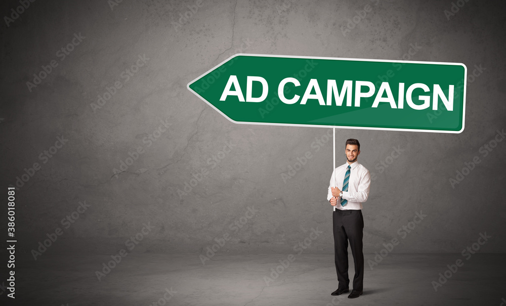 Young business person in casual holding road sign with AD CAMPAIGN inscription, new business direction concept Young business person in casual holding road sign with AD CAMPAIGN inscription, new business direction concept