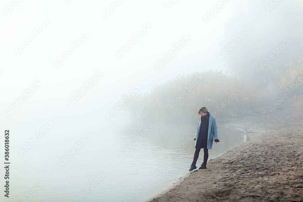 A girl runs along the shore of the lake in a foggy morning. She is having fun and has a good mood