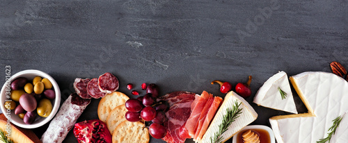 Assortment of cheese and meat appetizers. Top view bottom border on a slate stone banner background with copy space.