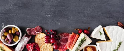 Panel kuchenny z motywem Assortment of cheese and meat appetizers. Top view bottom border on a slate stone banner background with copy space.