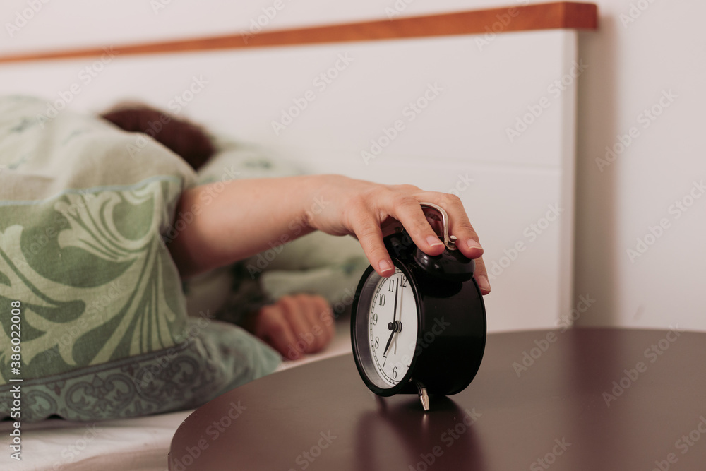 Caucasian woman in bed reaching out for analogue alarm clock to turn it