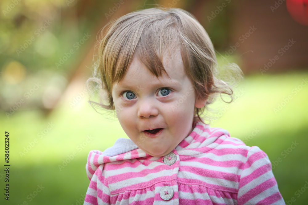 Close Up Portrait of a little 18 Month Old Girl with Big Blue Eyes and Curly Hair, a girl Playing Outside, Funny Face Expression, Happy baby Close Up Portrait of a little 18 Month Old Girl with Big Blue Eyes and Curly Hair, a girl Playing Outside, Funny Face Expression, Happy baby