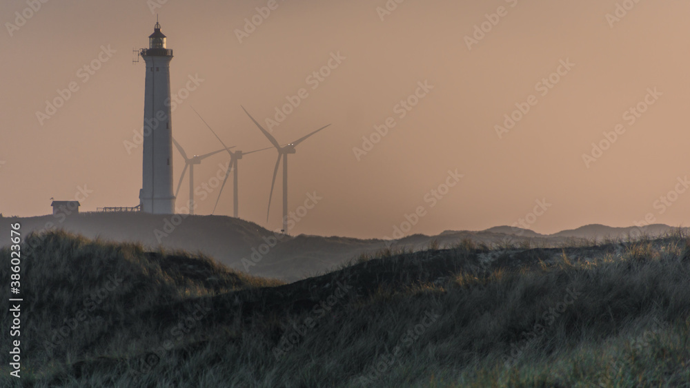 Drei Windkraftanlagen und ein Leuchtturm in der Abenddämmerung an der dänischen Nordseeküste