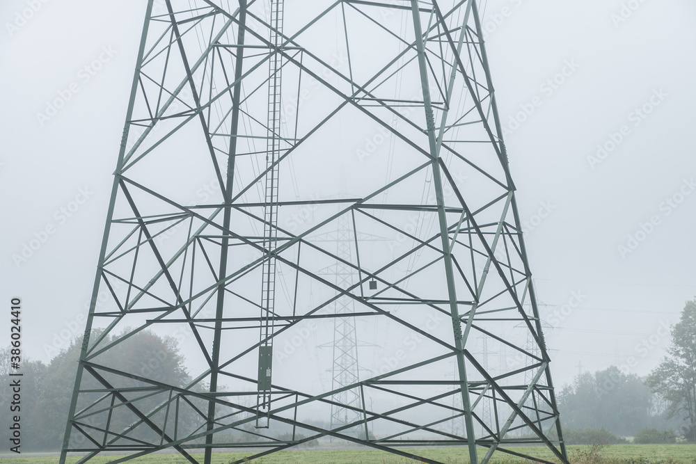 Close up view of electric power line towers align on farming field meadow. Hazy weather on flatland