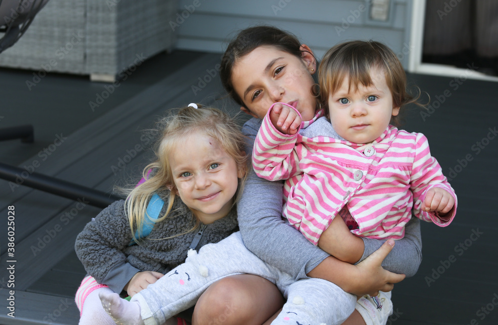 Three sister, girls sitting on the Porch. 3 girls, sisters, girlfriends. Happy Family Portrait, 18 month Old Toddler girl, 4 years Old blonde Girl and 9 years Old girl with brown hair Three sister, girls sitting on the Porch. 3 girls, sisters, girlfriends. Happy Family Portrait, 18 month Old Toddler girl, 4 years Old blonde Girl and 9 years Old girl with brown hair