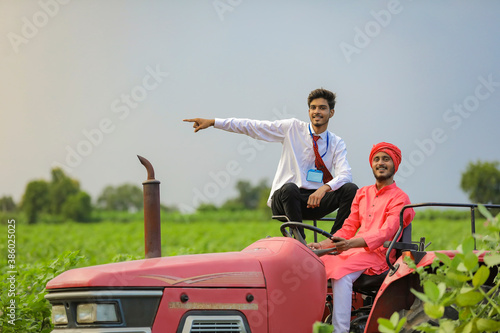 Young indian farmer and agronomist inspecting agriculture field on tractor
