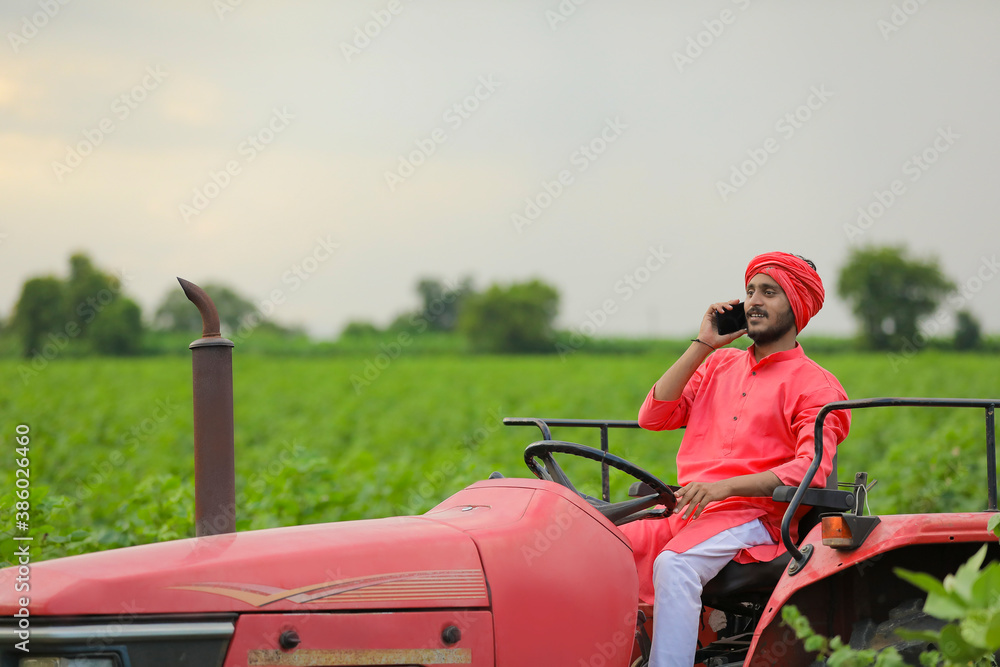 young indian farmer sitting on tractor and talking on smartphone at field young indian farmer sitting on tractor and talking on smartphone at field