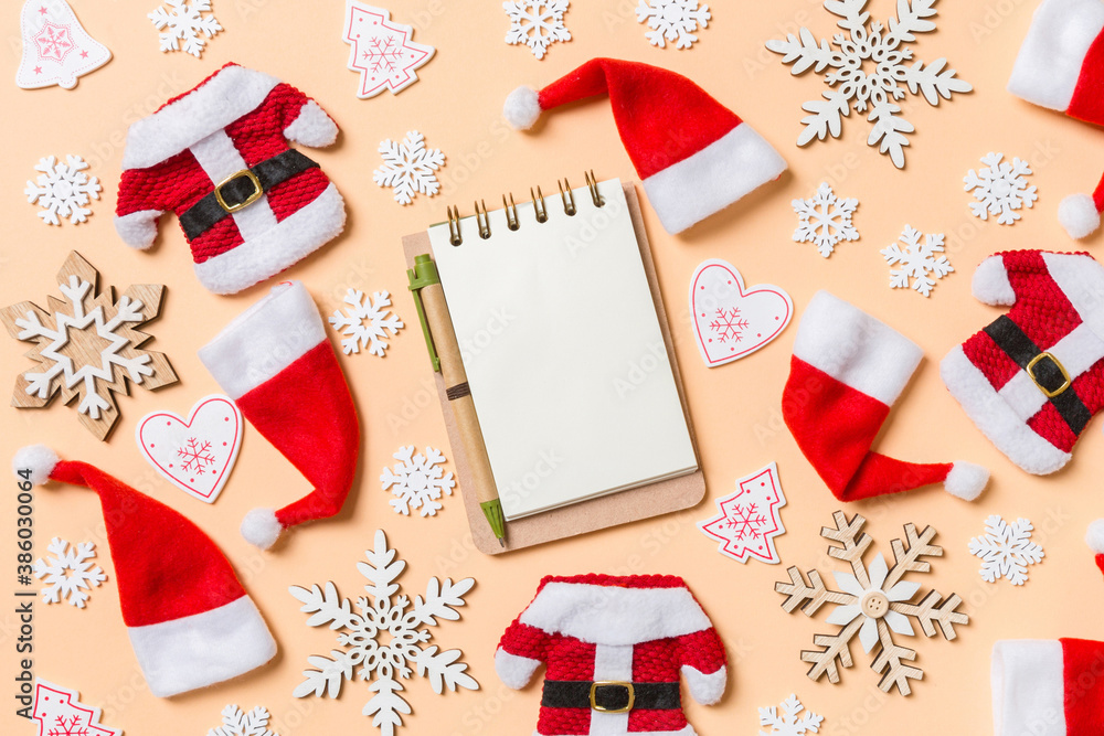 Top view of notebook with Christmas decorations and Santa hats on orange background. Happy holiday concept Top view of notebook with Christmas decorations and Santa hats on orange background. Happy holiday concept