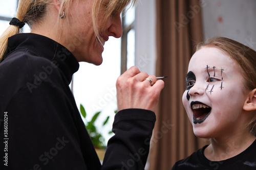 Mother is helping caucasuan daughter with Halloween makeup indoor photo