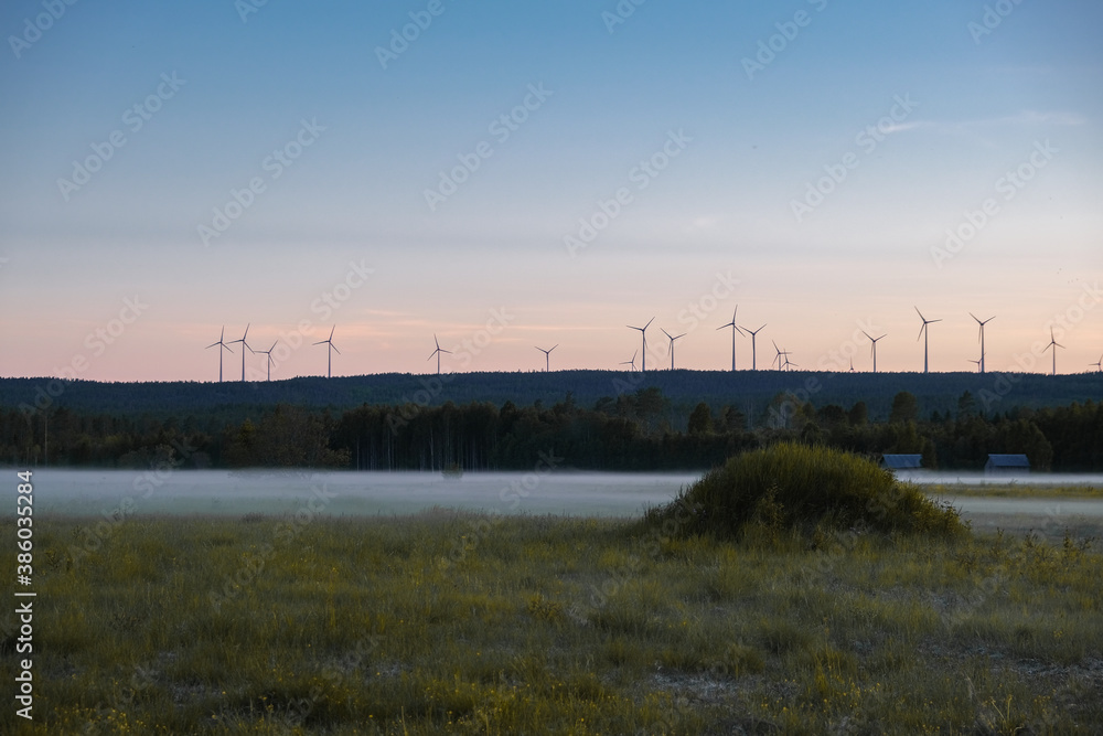 Sunset over a field, wind turbines and fog and spooky houses in the back in Sweden