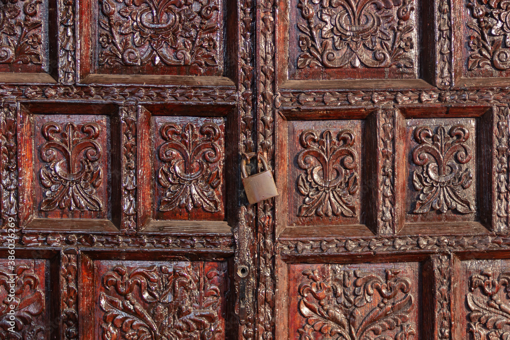 Puertas antiguas de madera labrada, sujetadas con armellas y un candado.