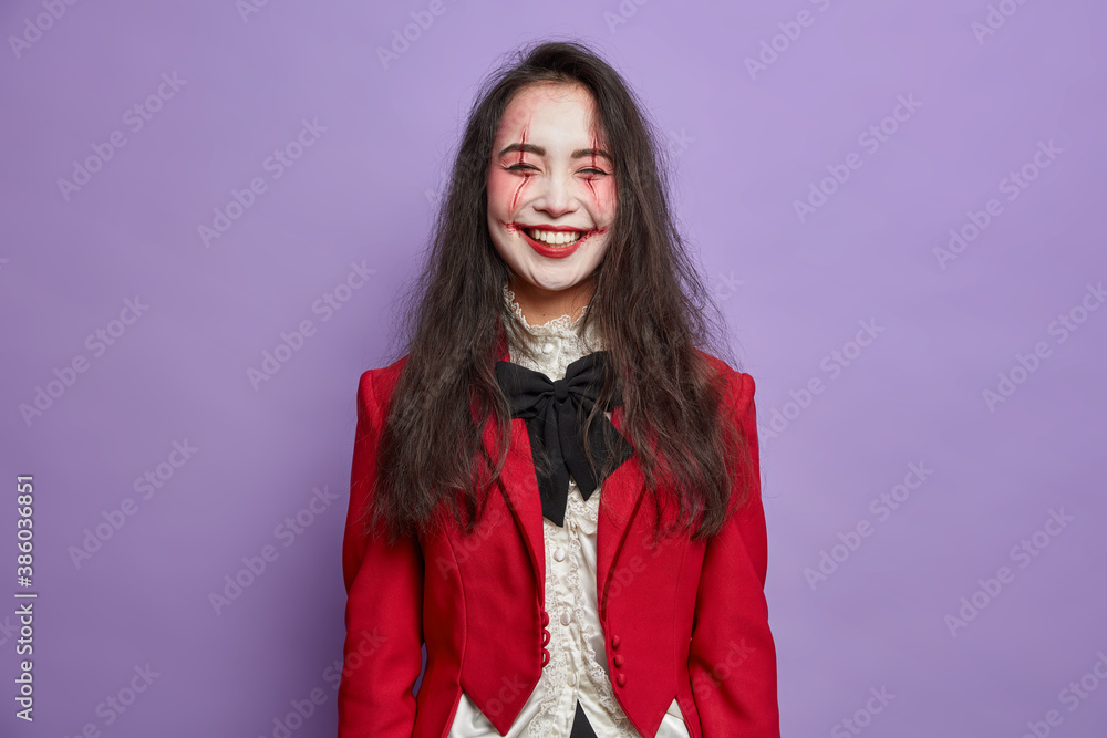 Φωτογραφία Overjoyed happy woman ghost celebrates halloween wears horrible makeup dressed in carnival costume poses against purple background