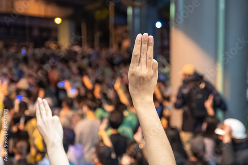 Thai People raise a hand three finger as the symbol of protesting for democracy in Thailand with blurred crowd background.