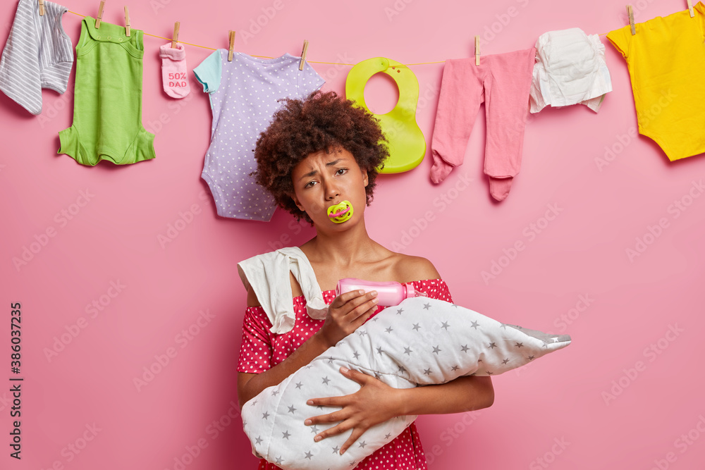 Φωτογραφία Young tired mother feeds baby from milk bottle keeps nipple in mouth poses with infant wrapped in blanket suffers from post natal depression feels exhausted of having sleepless nights