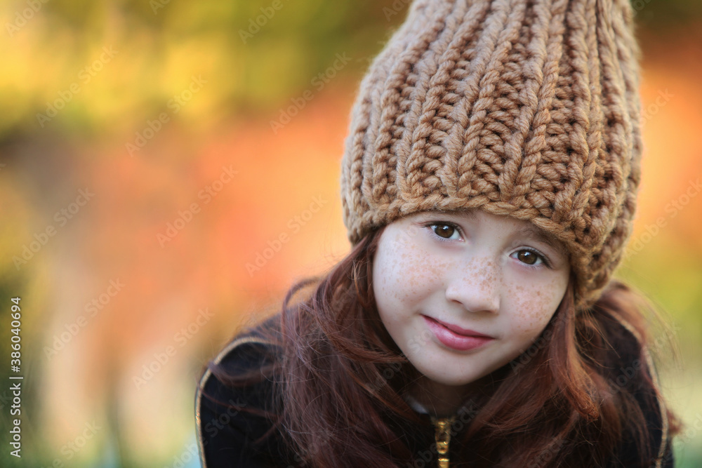 A girl in a warm knitted hat on the background of an autumn forest. Bokeh effect in the background. Headpiece for the cold season. A girl in a warm knitted hat on the background of an autumn forest. Bokeh effect in the background. Headpiece for the cold season.