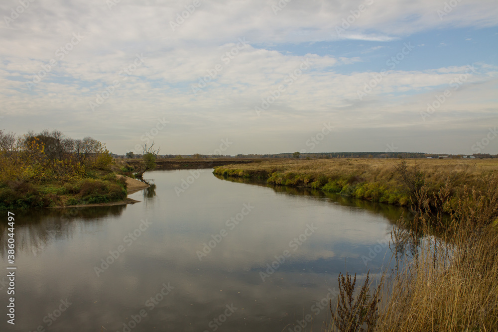 Autumn landscape - bend of the river with yellow grass and reflection of the cloudy sky and space for copying