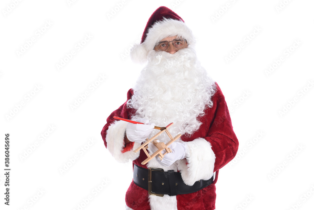 Senior man wearing a traditional Santa Claus costume painting a toy wooden airplane. Isolated on white. Senior man wearing a traditional Santa Claus costume painting a toy wooden airplane. Isolated on white.