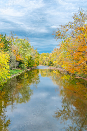 Yellow and orange fall colors of leaves on trees along river bank with reflections on water in autumn