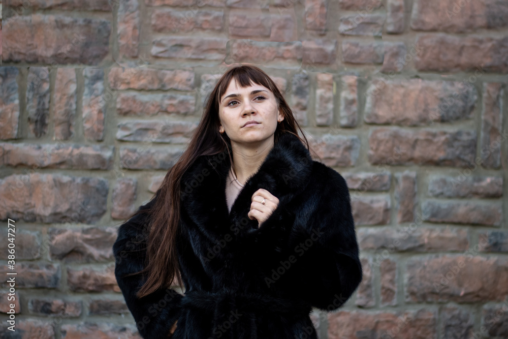 Young woman in a black mink coat near a stone wall. Beauty and fashion concept.