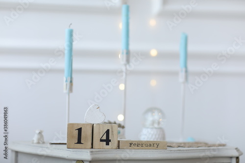 Valentine's day concept. Date 14 February on wooden cube calendar on a white gift box and white heart in hand. Bokeh golden and white background