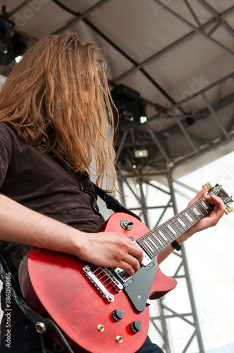 Red-haired guitarist plays the red electric guitar on the stage of the rock festival.