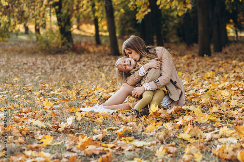 Happy mother and her beautiful daughter sitting and having fun among the yellow leaves in the autumn park.
