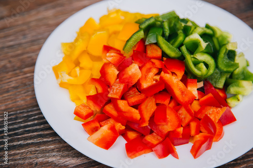 Red, yellow and green bell peppers, diced on a white plate. Dish on a wooden dark background