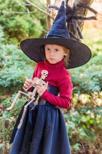 Little girl in a witch costume holding a skeleton on a halloween party