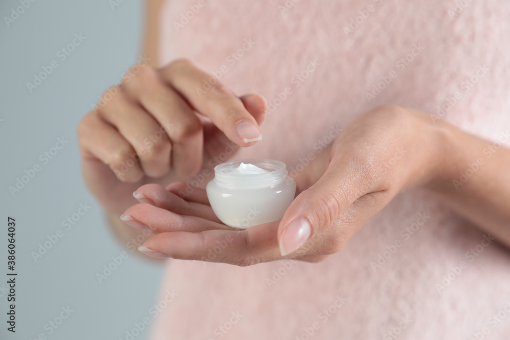 Young woman holding jar of cream on grey background, closeup Young woman holding jar of cream on grey background, closeup