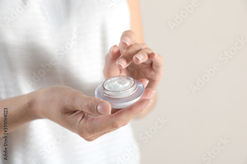 Young woman holding glass jar of cream on light background, closeup. Space for text