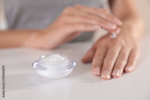 Young woman applying hand cream at table, closeup
