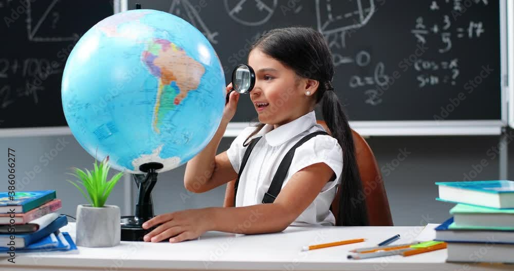 Cute little teen girl smiling and looking at world globe with magnifying glass at desk in classroom. Pretty small schoolgirl studying countries and geography. School concept. Cute little teen girl smiling and looking at world globe with magnifying glass at desk in classroom. Pretty small schoolgirl studying countries and geography. School concept.